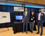 UW Master of Bioengineering students on the SoundCheck team standing at their table at a student competition. From left to right: Will Szymanski, Baolin Niu, Krishna Bathini