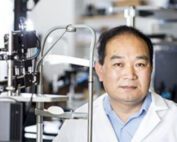 UW Bioengineering Professor Ruikang “Ricky” Wang wearing a lab coat in his lab standing next to a retinal camera