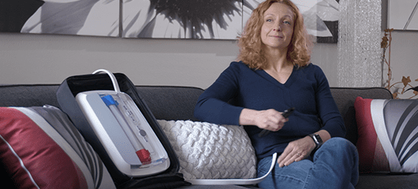 Woman sitting on sofa with portable kidney dialysis prototype next to her