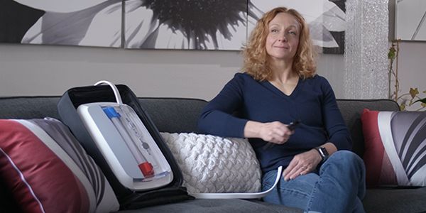 Woman sitting on sofa with portable kidney dialysis prototype next to her